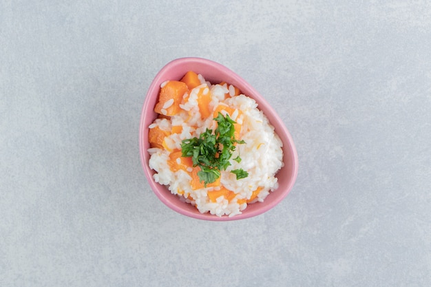 Prezzemolo affettato e riso alla carota nella ciotola, sullo sfondo di marmo.