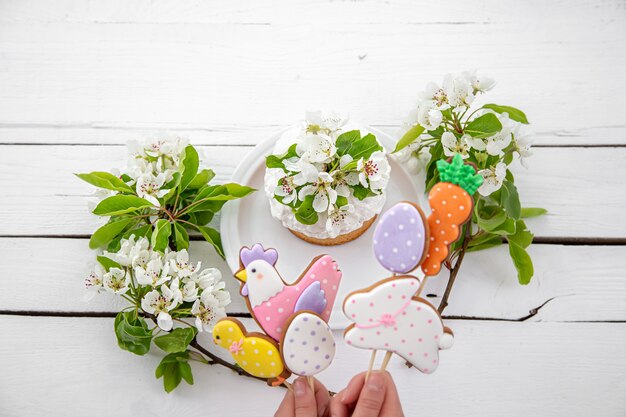 Primo piano dei biscotti luminosi del pan di zenzero di Pasqua sui bastoni e sulla torta di Pasqua decorata con i fiori. Il concetto di arredamento per le vacanze di Pasqua.