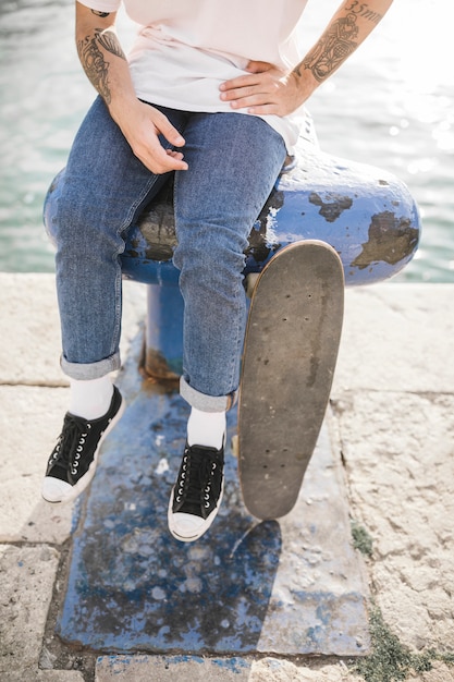 Primo piano dei piedi dell&#39;uomo con lo skateboard che si siede sulla bitta