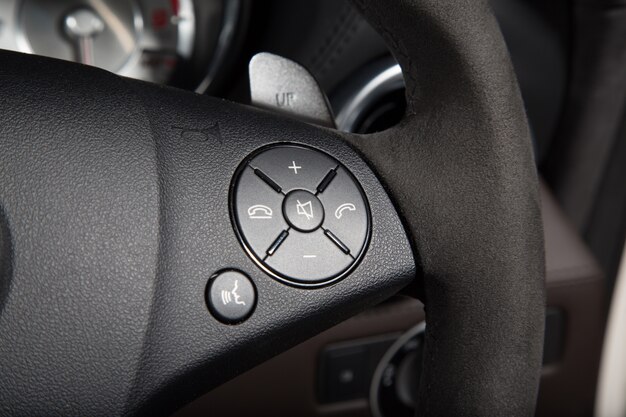 Primo piano dei pulsanti di controllo sul volante di un'auto di lusso sotto le luci