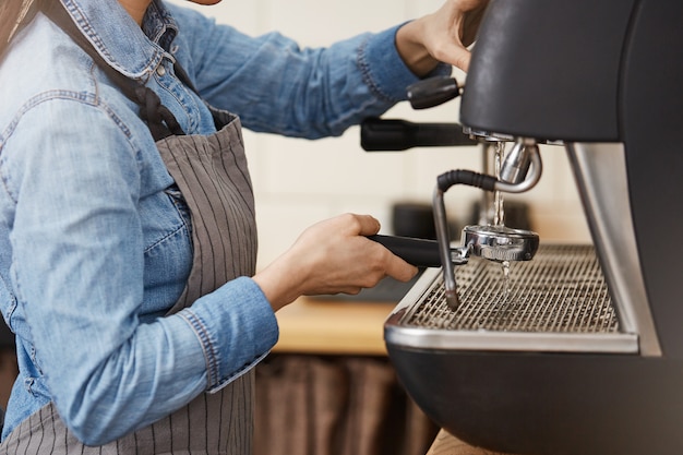 Primo piano del barista femminile che pulisce portafilter senza fondo con il vapore.