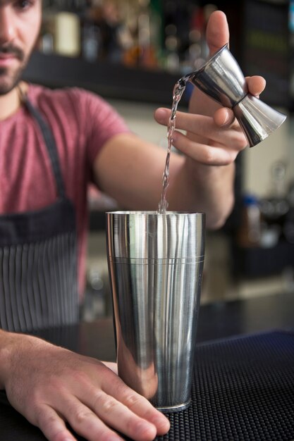 Primo piano del barista versando cocktail in shaker al bancone del bar