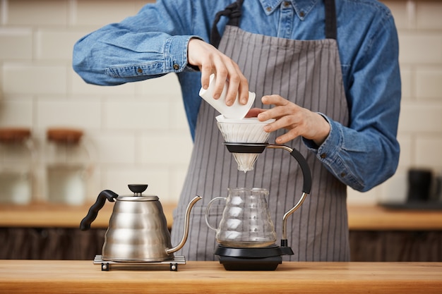 Primo piano del caffè macinato di versamento di barista maschio che produce pouron.