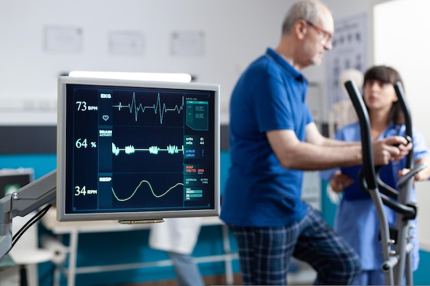 Primo piano del cardiofrequenzimetro che misura il battito cardiaco per il paziente che fa ginnastica per il recupero fisico. Uomo in pensione che utilizza attrezzature sportive per esercitarsi per fisioterapia e forza.