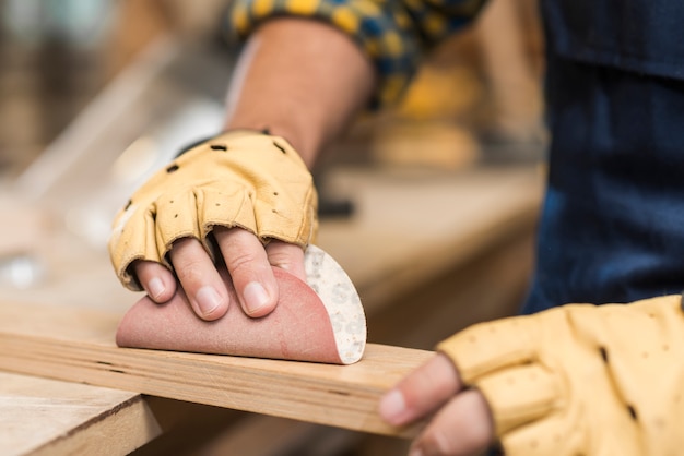 Primo piano del carpentiere maschio che sfrega legno con carta vetrata