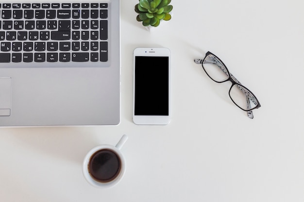 Primo piano del computer portatile e del telefono cellulare con la tazza di caffè e gli occhiali