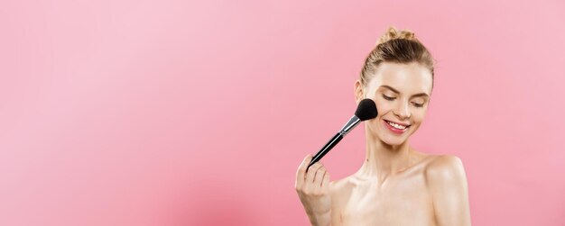 Primo piano del concetto di bellezza Bella donna caucasica che applica il trucco con la spazzola cosmetica per polvere Pelle perfetta isolata su sfondo rosa e spazio per la copia