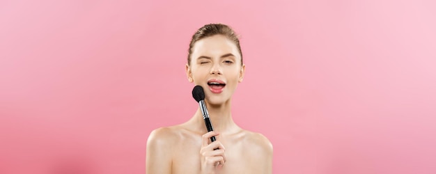 Primo piano del concetto di bellezza Bella donna caucasica che applica il trucco con la spazzola cosmetica per polvere Pelle perfetta isolata su sfondo rosa e spazio per la copia