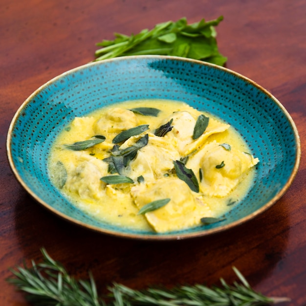 Primo piano del contorno squisito della pasta dei ravioli con la foglia del basilico sulla tavola di legno