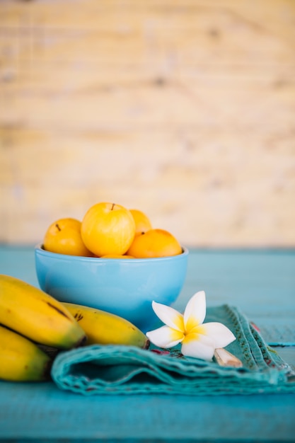 Primo piano del fiore bianco; banana e prugne sul tavolo in legno blu