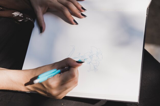 Primo piano del fiore del disegno della donna con la penna colorata blu sul taccuino