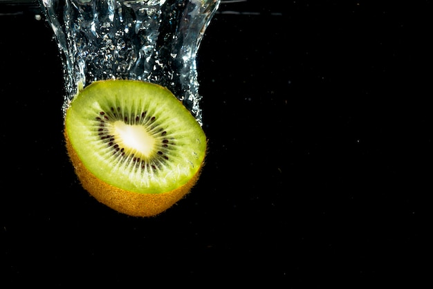 Primo piano del kiwi diviso in due che cade con la spruzzata dell&#39;acqua