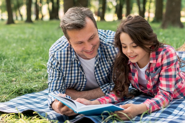 Primo piano del libro di lettura sorridente della figlia e del padre mentre trovandosi sulla coperta al parco