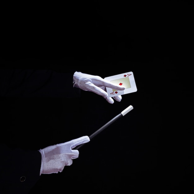 Primo piano del mago che esegue il trucco sulla carta da gioco con la bacchetta magica