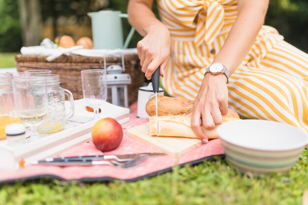 Primo piano del pane di taglio della donna con il coltello sul picnic