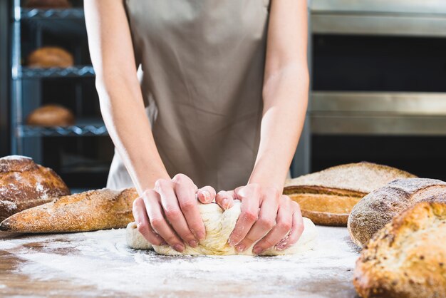 Primo piano del panettiere femminile che impasta la pasta con farina su superficie di legno