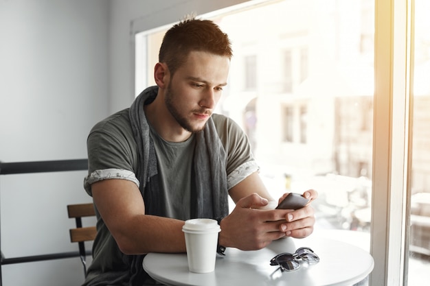 Primo piano del ragazzo seduto al tavolo di caffè, messaggio SMS.