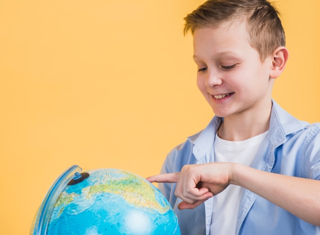 Primo piano del ragazzo sorridente che tocca il globo con il dito contro fondo giallo