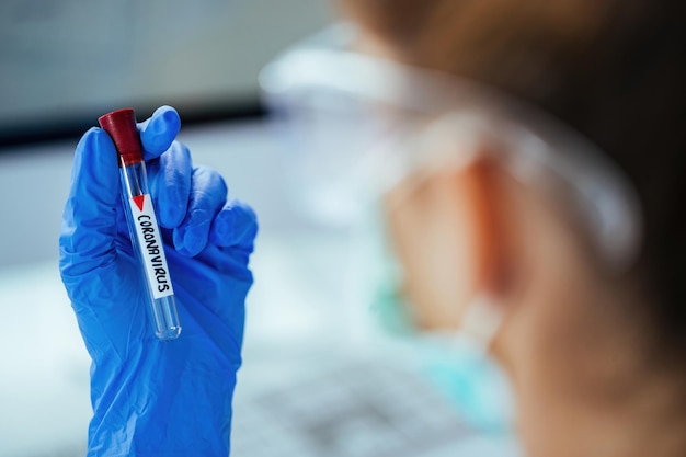 Primo piano del tecnico medico che tiene la provetta con coronavirus mentre lavora in laboratorio