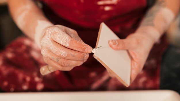 Primo piano del vasaio femminile che pulisce la pittura sulle mattonelle con lo strumento tagliente