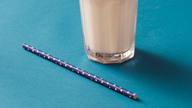 Primo piano del vetro di latte con la cannuccia del pois sul contesto blu