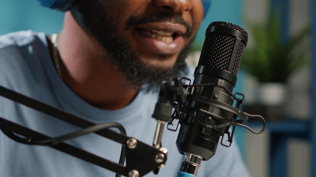 Primo piano del vlogger afroamericano che utilizza il microfono per la conversazione con gli abbonati sul podcast dei social media. Influencer nero che lavora con attrezzature moderne per la trasmissione online