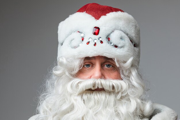 Primo piano del volto di Babbo Natale con cappello rosso, uomo stanco con i capelli grigi