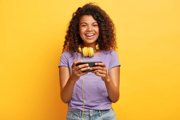 Primo piano del volto di bella giovane femmina con acconciatura afro in posa contro il muro giallo