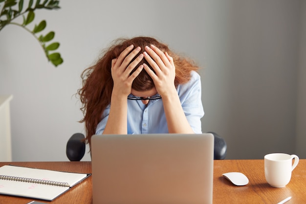 Primo piano del volto di impiegato femminile esausto rossa in camicia blu e bicchieri