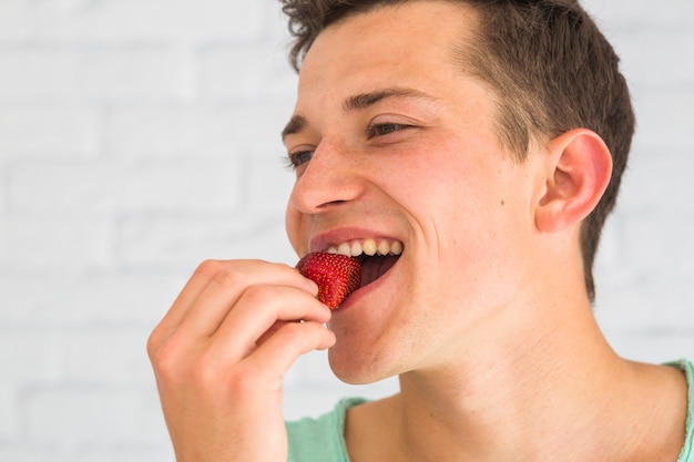 Primo piano del volto di un uomo che mangia fragola rossa