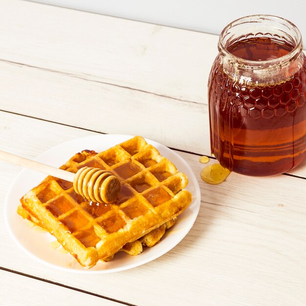 Primo piano del waffle e del miele squisiti in zolla su superficie di legno