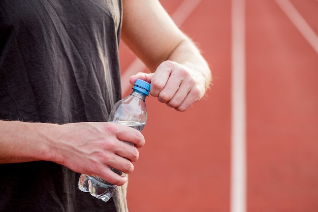 Primo piano dell'atleta che apre la bottiglia di acqua di plastica