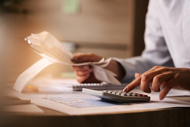 Primo piano dell'economista che utilizza la calcolatrice mentre esamina le bollette e le tasse in ufficio