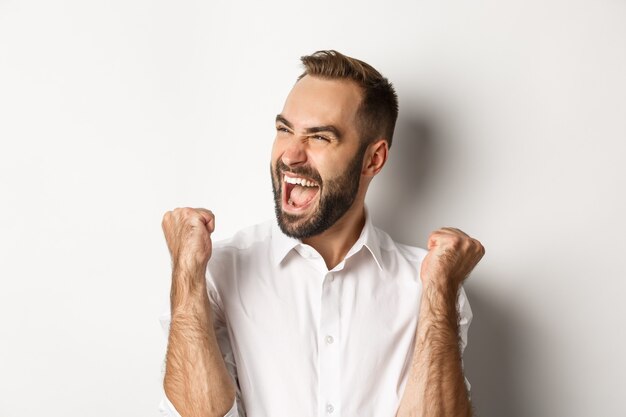 Primo piano dell'uomo caucasico di successo che si rallegra, facendo pompare il pugno e gridando di gioia, guardando a sinistra, vincendo, in piedi