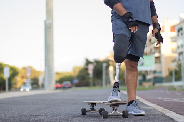 Primo piano dell'uomo con la gamba protesica e lo skateboard. Persona forte con disabilità in abiti casual su skateboard, nessuno in giro. Sport, disabilità, concetto di hobby