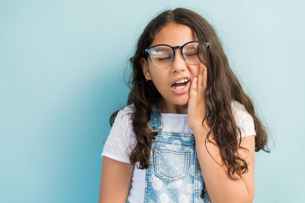 Primo piano della bambina a disagio con la mano sulla guancia che soffre di mal di denti in studio