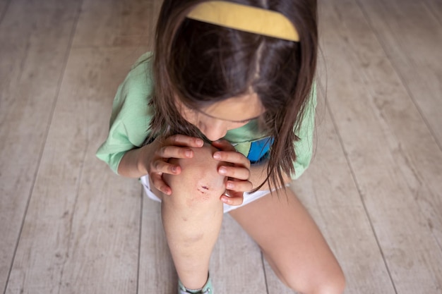 Primo piano della bambina che tiene il suo ginocchio danneggiato ferito ferito con le mani