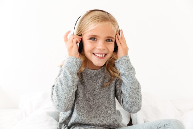 Primo piano della bambina sorridente graziosa che tocca le sue cuffie mentre ascoltando la musica,