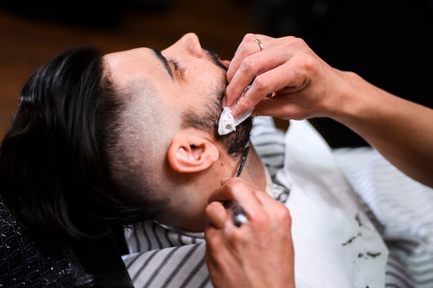 Primo piano della barba del cliente di taglio del barbiere di vista laterale