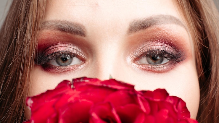 Foto gratuito primo piano della bella parte superiore femminile del viso giovane ragazza bruna che nasconde il naso e la bocca dietro i fiori rossi bella signora con trucco luminoso che tiene le rose concetto di pubblicità di cosmetici