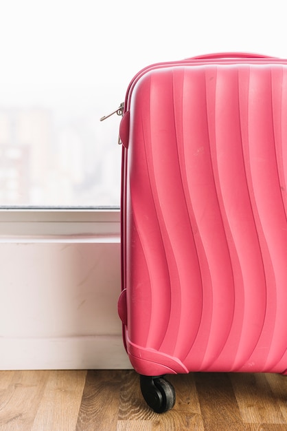 Primo piano della borsa da viaggio rosa con ruote sul pavimento di legno vicino alla finestra