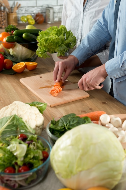 Primo piano della carota del taglio manuale dell&#39;uomo sul tagliere con il coltello sul contatore di cucina di legno