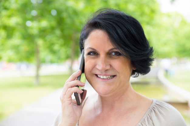 Primo piano della donna allegra che parla sulla cellula all'aperto