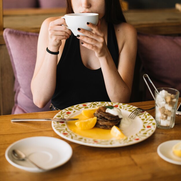 Primo piano della donna che beve caffè con il dessert sul piatto