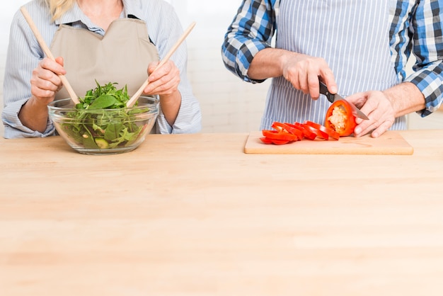 Primo piano della donna che prepara l&#39;insalata e suo marito che tagliano il peperone dolce sulla tavola di legno