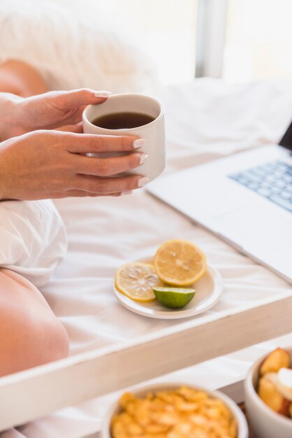 Primo piano della donna che si siede sul letto che tiene tazza di caffè in mano