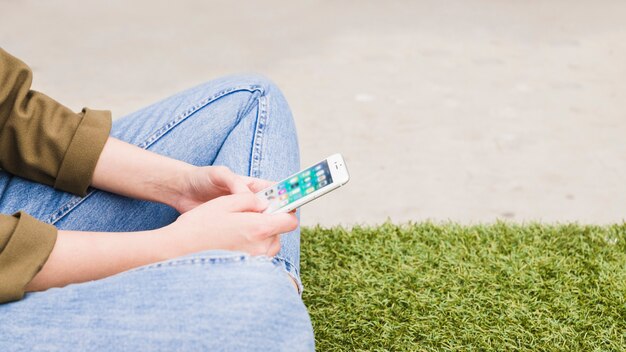 Primo piano della donna che si siede sull&#39;erba verde utilizzando social media app sul cellulare