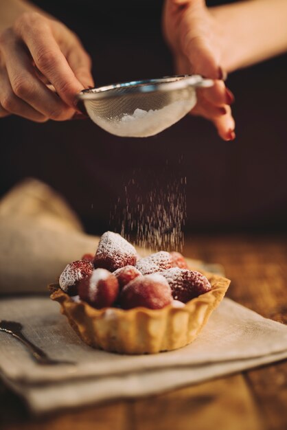 Primo piano della donna che spolvera la polvere dello zucchero sulla crostata della fragola