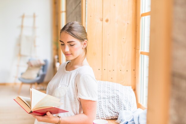 Primo piano della donna che sta vicino al libro di lettura della finestra