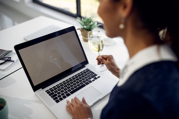 Primo piano della donna che usa il computer portatile mentre beve vino in ufficio